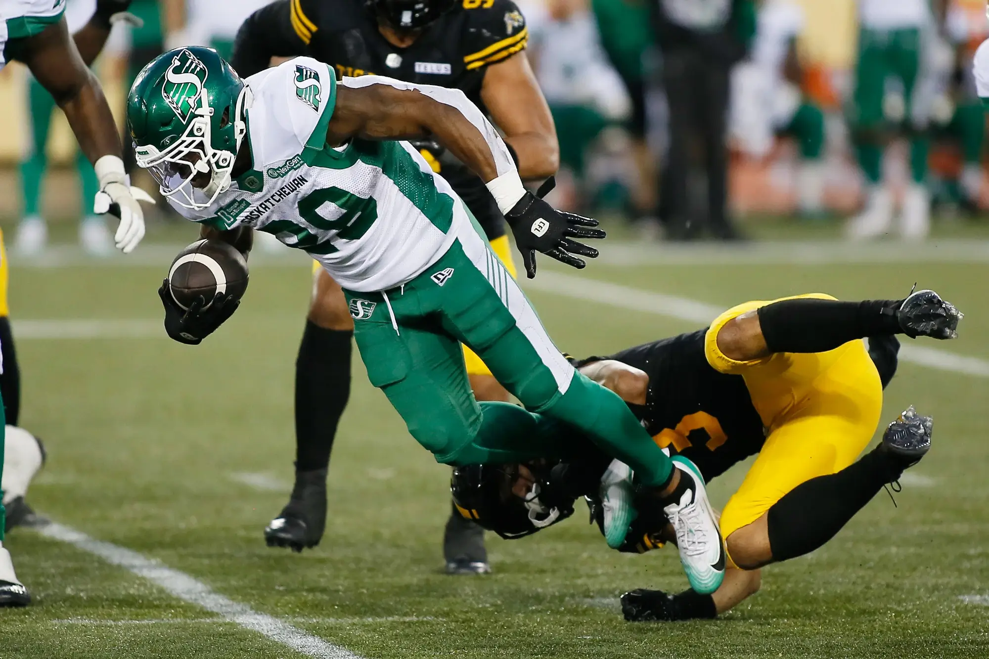 Jun 14, 2025; Hamilton, Ontario, Canada; Saskatchewan Roughriders running back Ka'Deem Carey (29) gets tripped up by Hamilton Tiger-Cats defensive back Branden Dozier (3) at Hamilton Stadium. 
