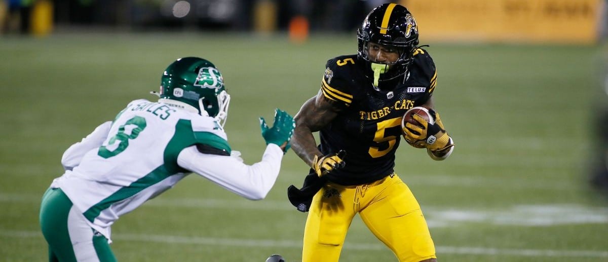 Hamilton Tiger-Cats running back Greg Bell (5) tries to avoid a tackle from Saskatchewan Roughriders defensive back Marcus Sayles (8) at Hamilton Stadium