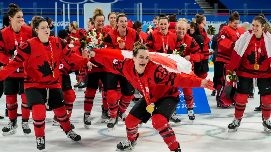 Team Canada captain Marie Philip Poulin celebrates with the Canadian flag and her teamates after winning gold at the 2022 Beijing Olympics.