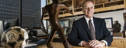 Alan Rothenberg seated at his desk with a signed soccer ball and bronze trophy