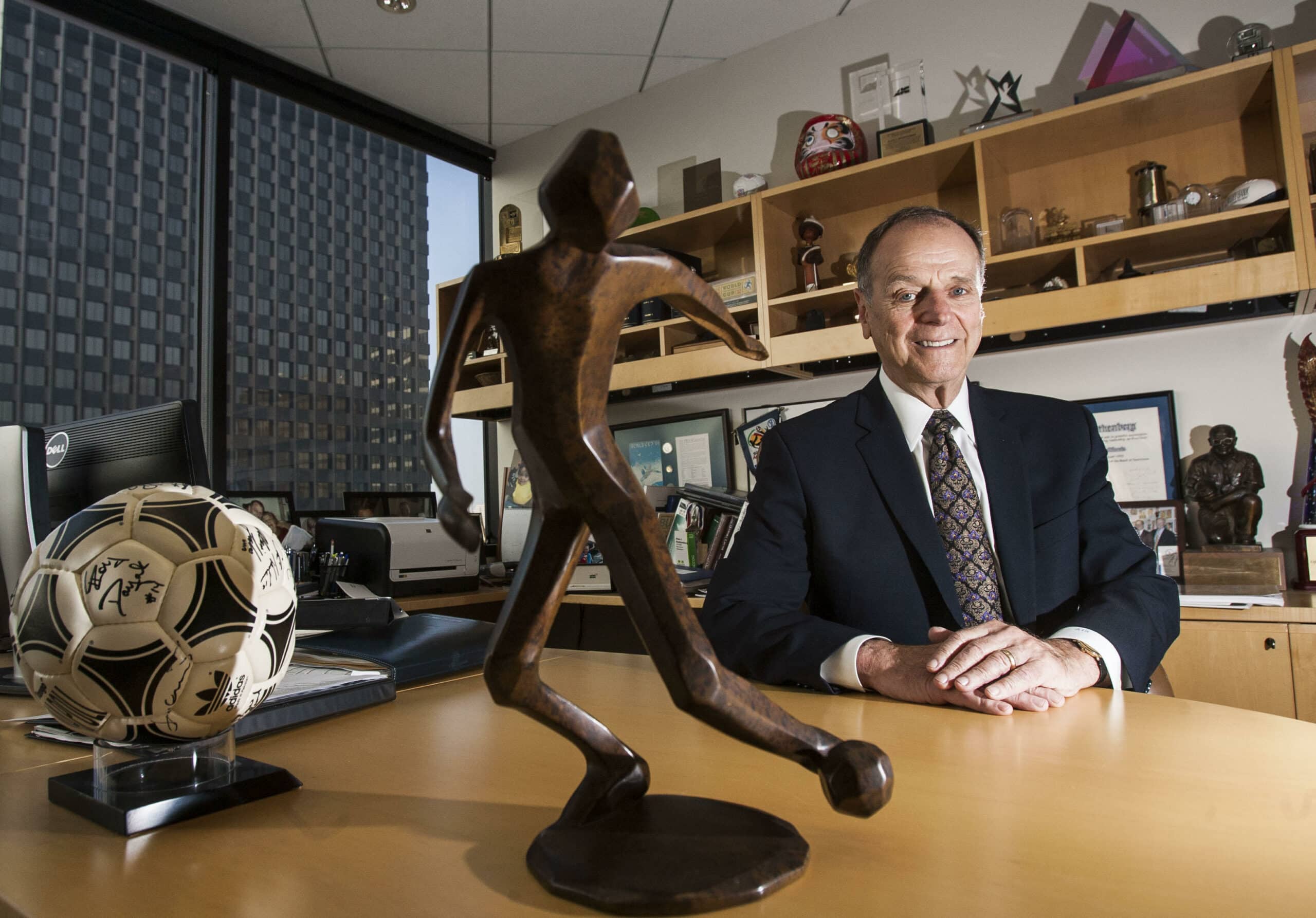Alan Rothenberg seated at his desk with a signed soccer ball and bronze trophy