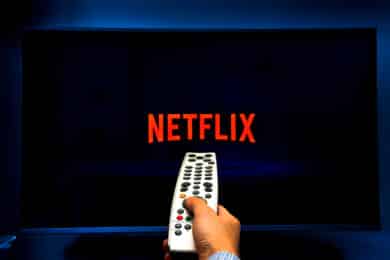 Male hand holding a remote control while watching Netflix on a TV screen