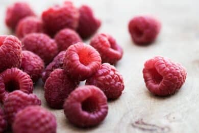 Close-up of fresh red raspberries scattered on a pale wooden board.