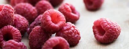 Close-up of fresh red raspberries scattered on a pale wooden board.